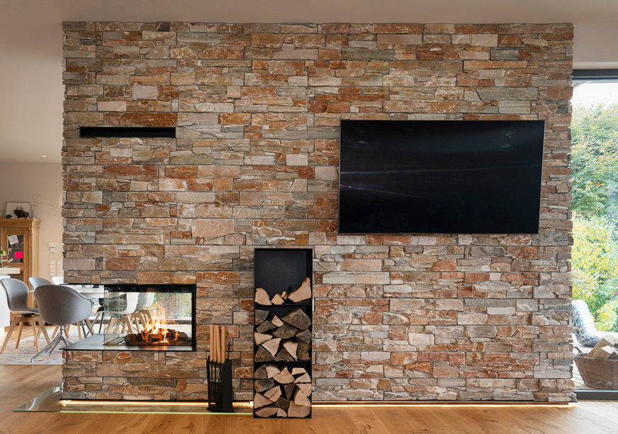 Gut zu sehen, wie die Lichtstreifen in den Schattenfugen eine schöne Stimmung in den Raum zaubern. Die Wand bietet sogar Platz fürs Kaminbesteck, ein Feuerholzregal und einen großen Fernseher.