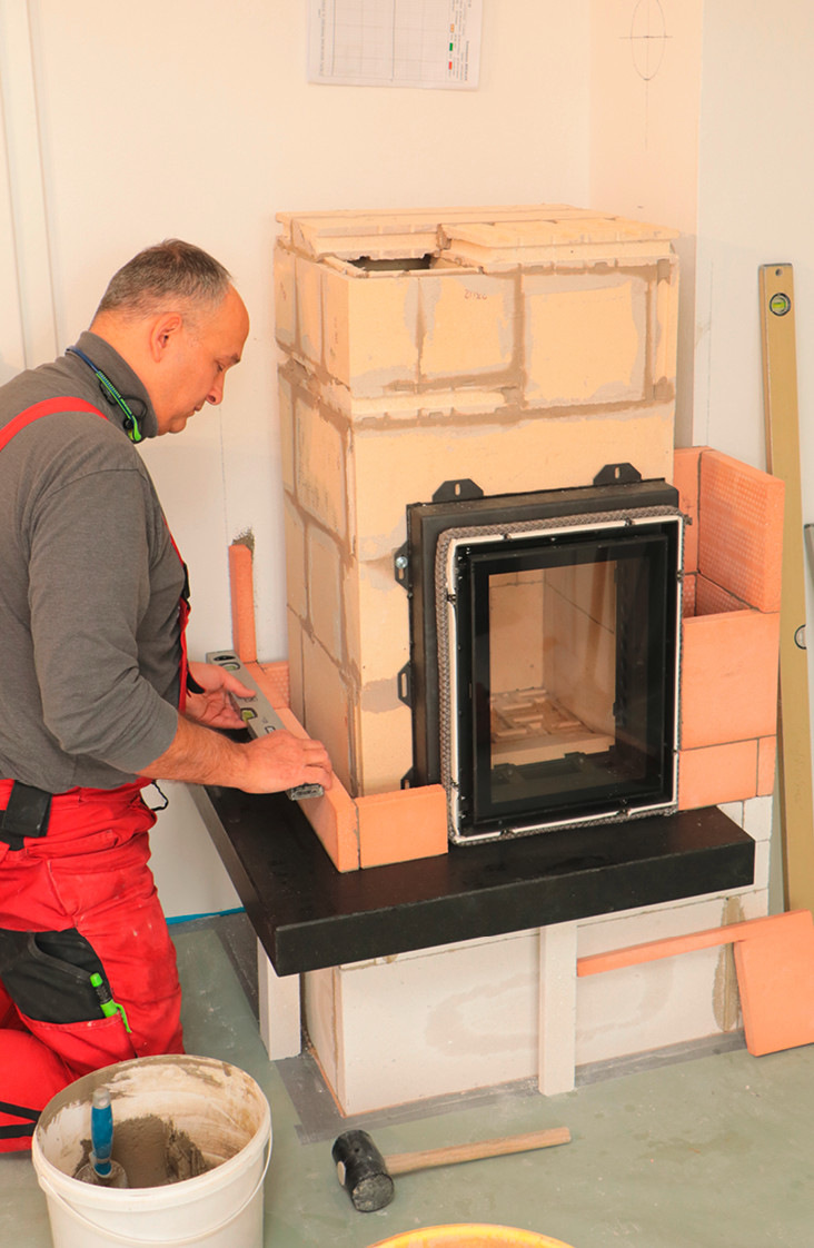 Jetzt ist die rings um den Grundofenkern herumlaufende Ofenhaut an der Reihe. Diese wird ebenfalls mit wärmespeichernden Schamotteplatten hergestellt. Gut zu erkennen: Der Ofensetzer hält hierbei stets einen Abstand von mindestens zwei Zentimetern zum Ofenkern ein, so erfolgt durch die „stehende Luftschicht“ ein guter Wärmeübergang vom Ofenkern an die Ofenhaut.