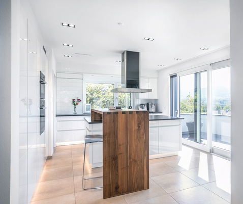 Die geräumige Küche mit Kochinsel und Frühstückstheke ist über Fensterschiebetüren mit dem Balkon verbunden.