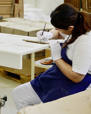 Manufakturarbeit. Hier trägt eine Mitarbeiterin Majolika-Glasur mit dem feinen Pinsel von Hand auf.