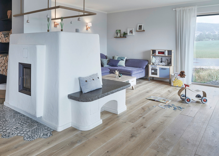 Mittelpunkt des Wohnraumes ist der weiße Ofen. - © Foto: BauFritz