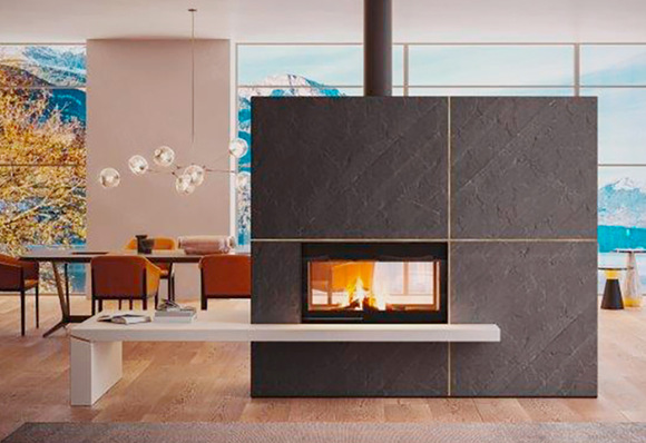 Das beidseitige Modell  „WT  16:9 ”  mit einer neuen Verkleidung, deren Entwurf ganz auf die Aufwertung des Designs ausgerichtet ist: eine Verkleidung mit Bank aus matt geschliffenem Marmor Bianco Mediterraneo mit Dekoreinsatz aus Metall, die auf der mit schwarzem Schieferstein verkleideten Stauraumwand der Feuerstätte aufliegt.